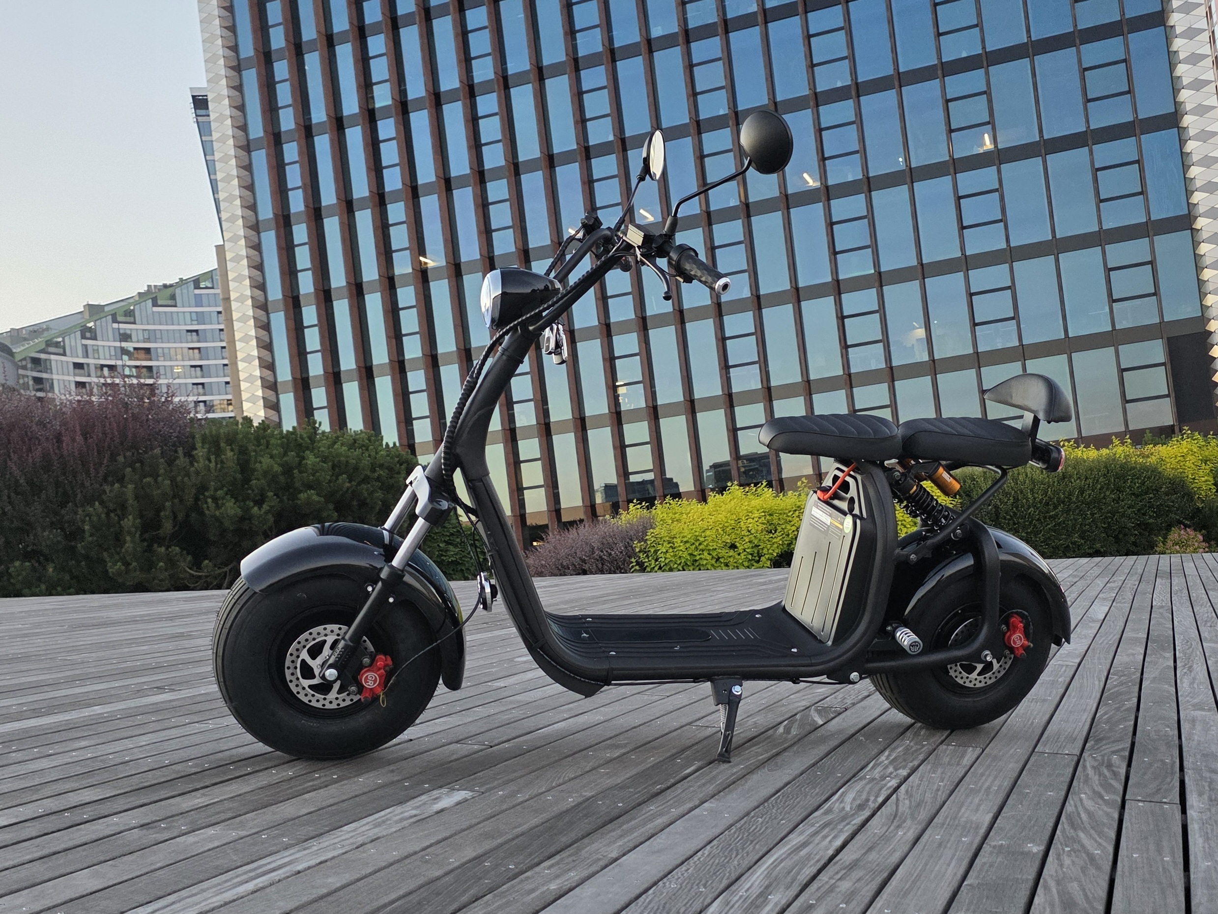Juodas CityCoco elektrinis čioperis (elektrinis motoroleris) su plačiomis padangomis miesto fone