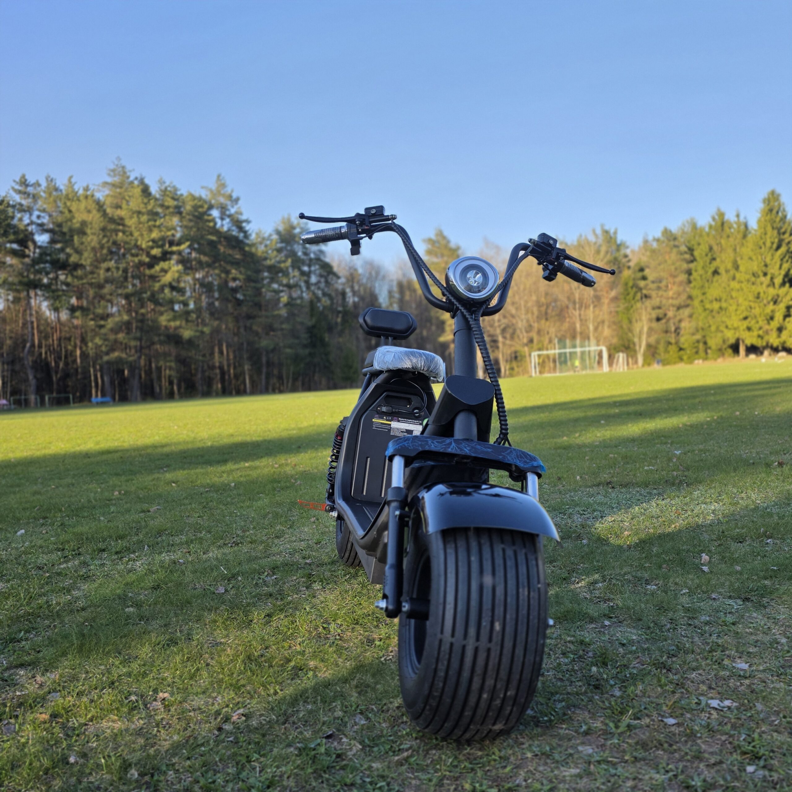 Juodas CityCoco elektrinis motoroleris su plačiomis padangomis pavasario peizažo fone